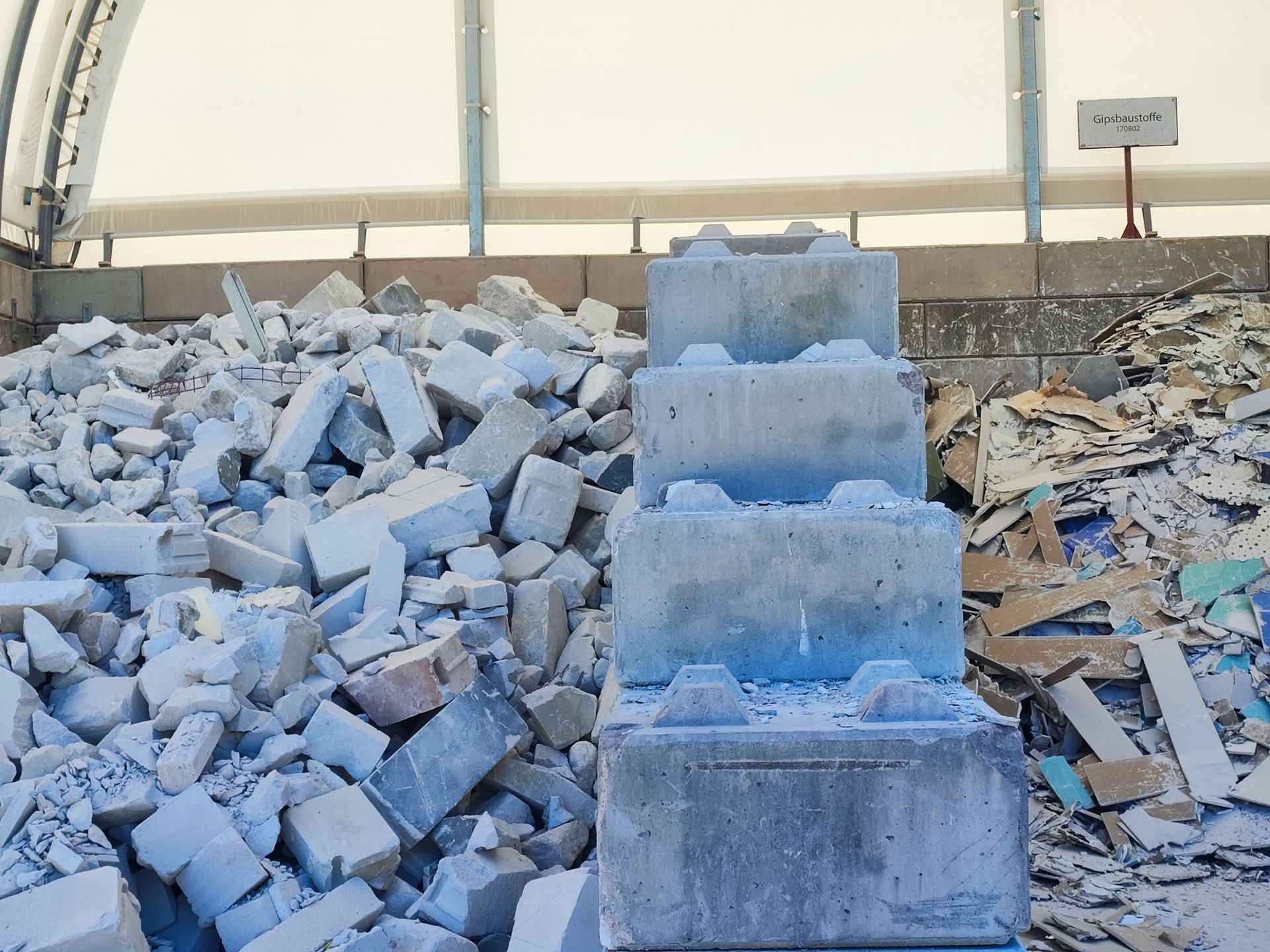 Pile of concrete rubble and large cement blocks inside a covered industrial area.